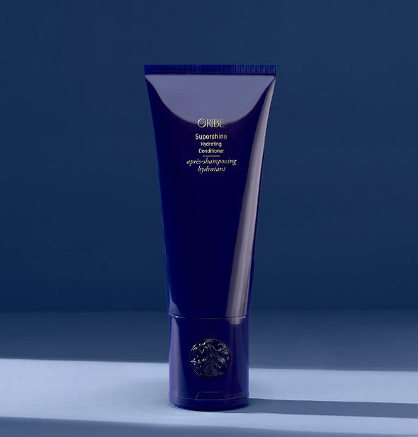 Dark blue 6.8 ounce bottle of Oribe Supershine Hydrating Conditioner on a dark blue shadowy backdrop