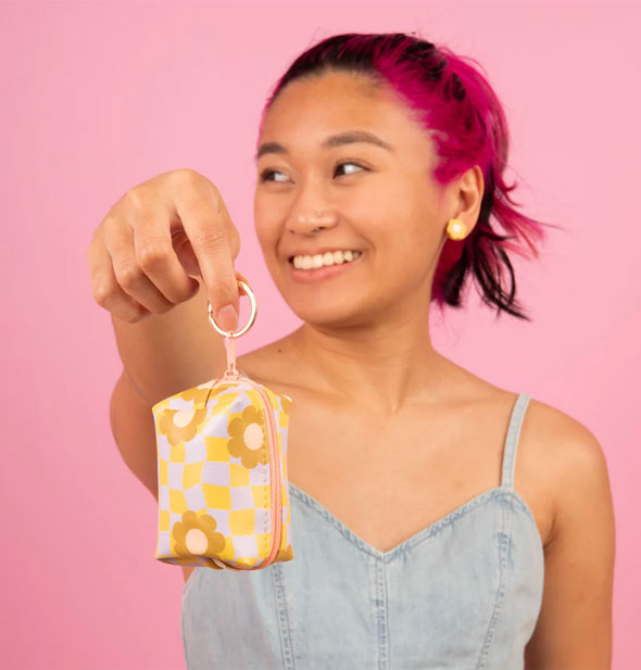 Smiling model holds a Cool Funky Daisy Tag-a-Long Key Ring pouch out toward camera in front of a pink backdrop