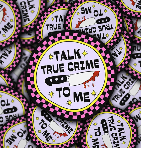 Pile of round stickers that say, "Talk true crime to me" in black lettering accented by yellow stars around a bloody knife graphic inside a black, pink, and yellow checker border