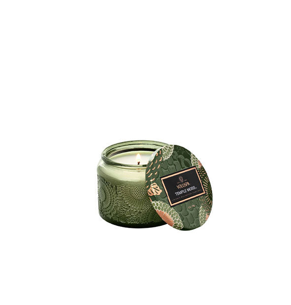 Green embossed glass Voluspa Temple Moss candle with green, gold, and cream floral patterned tin lid removed and resting against it