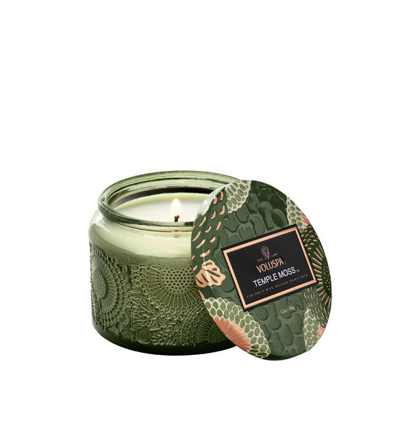 Green embossed glass Voluspa Temple Moss candle with green, gold, and cream floral patterned tin lid removed and resting against it
