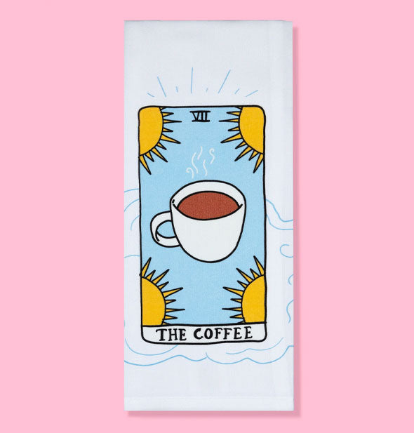 White dish towel on pink background features tarot card-style artwork featuring a coffee cup surrounded by four yellow suns and the caption, "The Coffee" below