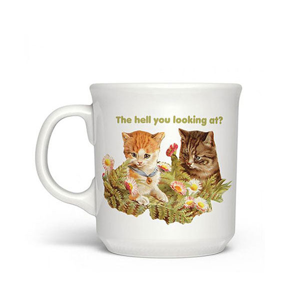 White coffee mug featuring an illustration of two kittens surrounded by ferns and flowers says, "The hell you looking at?" in green lettering