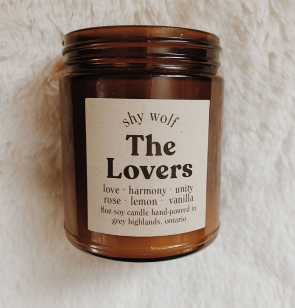 Shy Wold 8 oz. amber glass jar soy candle on white fur surface says, "The Lovers: Love, harmony, unity, rose, lemon, vanilla" on the label