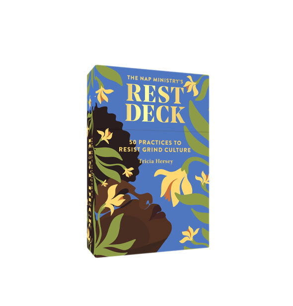 Predominantly blue box of The Nap Ministry's Rest Deck features gold lettering and an illustration of the profile a black femme with afro emerging from a covering of yellow flowers and green leaves