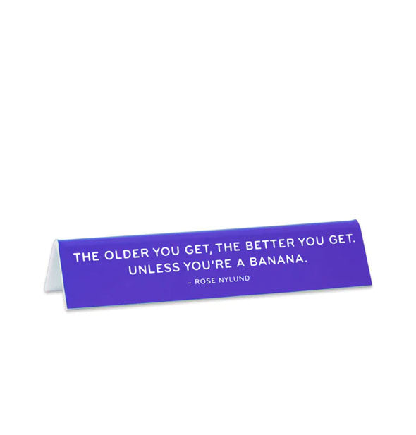 Rectangular purple desk sign says, "The older you get, the better you get. Unless you're a banana. - Rose Nylund" in white lettering