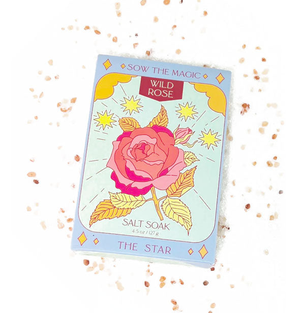 Packet of Wild Rose Salt Soak is surrounded by scattered salt granules and features a vibrant rose illustration in the style of The Star tarot card