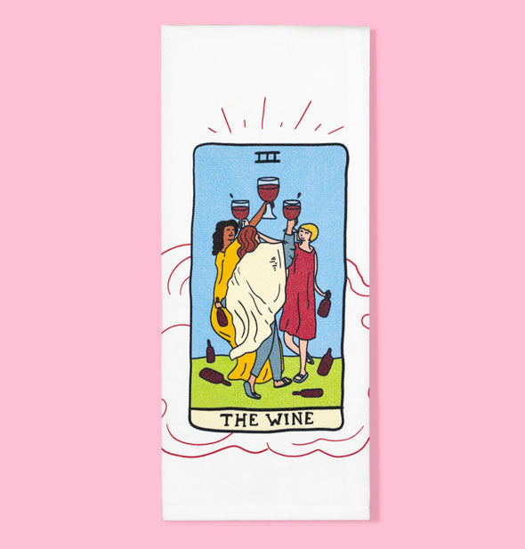 White dish towel on pink background features tarot card-themed illustration featuring three people holding up goblets of red wine with bottles strewn around them and the caption, "The Wine" below