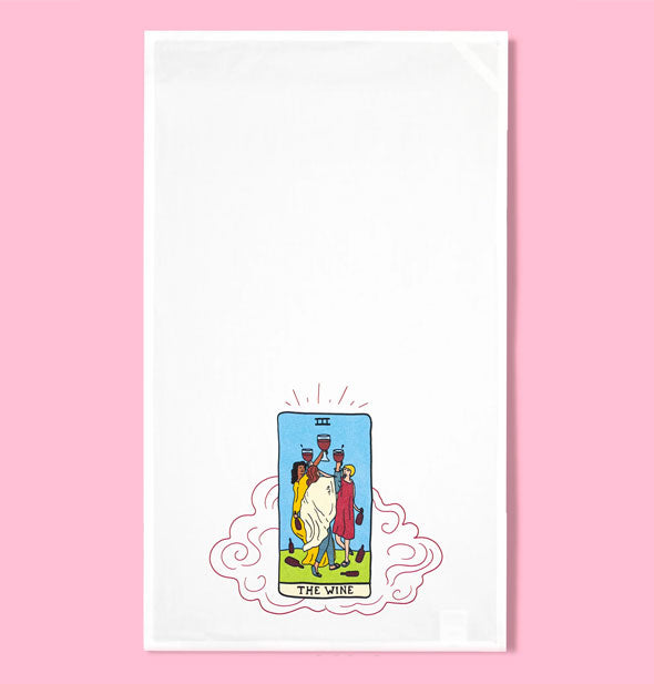 White dish towel on pink background features tarot card-themed illustration featuring three people holding up goblets of red wine with bottles strewn around them and the caption, "The Wine" below