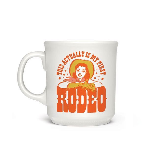 White coffee mug with gold and orange illustration of a cowgirl accented by stars says, "This actually is my first rodeo" in a Western-style typeface