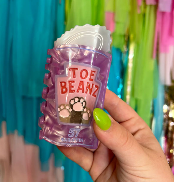 Model's hand holds a Toe Beanz claw clip with cat paws design in front of a colorful streamer backdrop