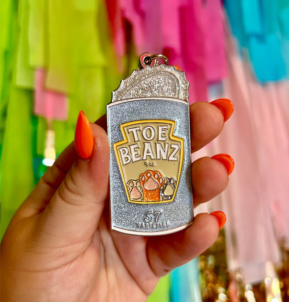 Model's hand holds a glittery Toe Beanz keychain designed as an opened food can with cat paws on the label