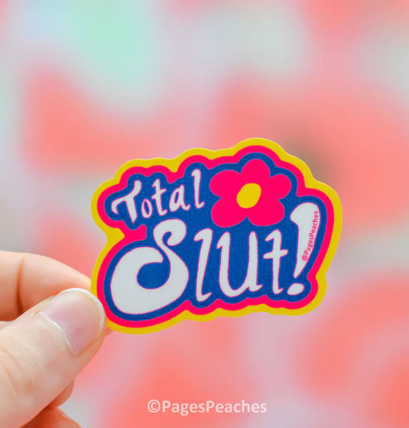 Model's hand holds a sticker that says, "Total Slut!" with a pink and yellow flower on a blue background with pink and yellow border