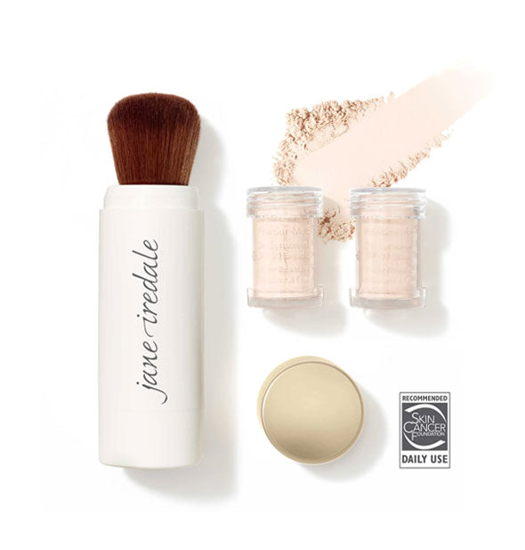 White Jane Iredale powder brush, two clear refill canisters, and gold cap are spaced out with a sample of swiped powder sunscreen in shade Translucent