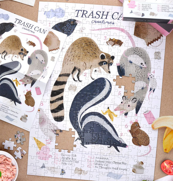 A mostly assembled Trash Can Creatures jigsaw puzzle is staged with reference sheet, box, loose pieces, and random food scraps