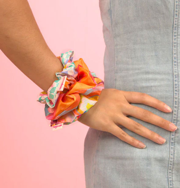 Model wears three scrunchies from the Trippy Dippy set on right wrist with hand on hip