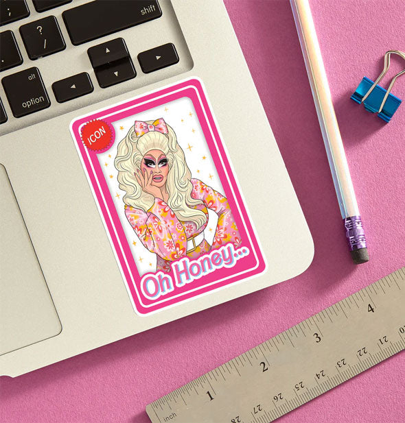 Trixie Mattel sticker is applied to a laptop that is staged with a pencil, ruler, and blue binder clip on a pink surface