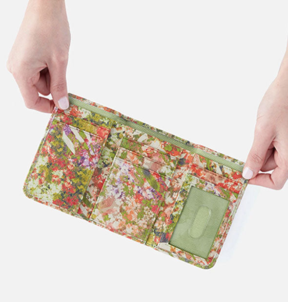 Model's hands hold open a small multicolored tropical floral print trifold wallet to show storage slots inside