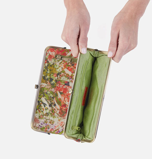 Model's hands hold open a section of tropical print wallet with green interior and brass frame hardware