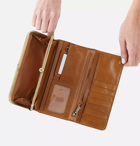 Model's hands hold open a brown leather wallet with gold hardware to reveal pockets and compartments inside