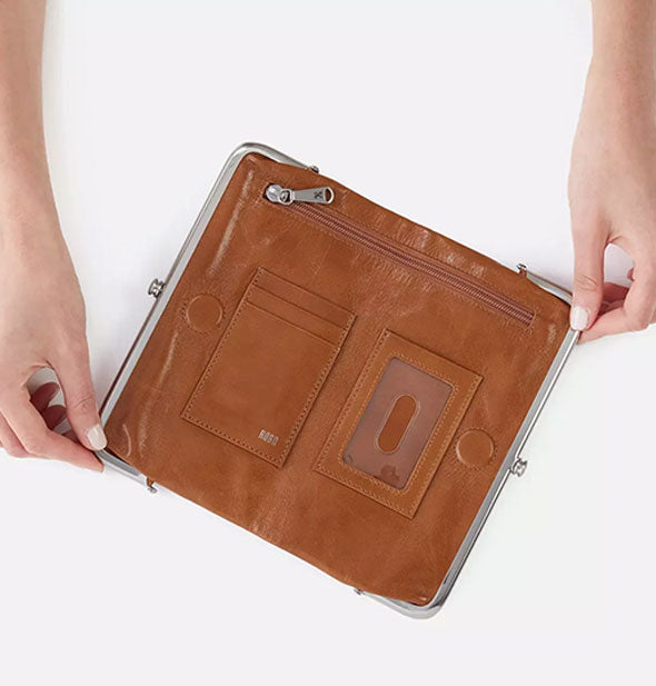 Model's hands hold open a brown leather wallet to reveal slots and pockets inside