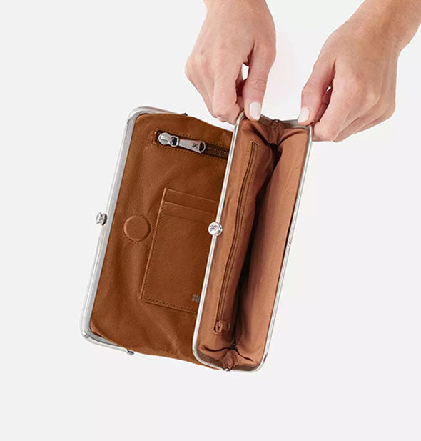 Model's hands hold open a section of a brown leather wallet to reveal an interior zipper pocket