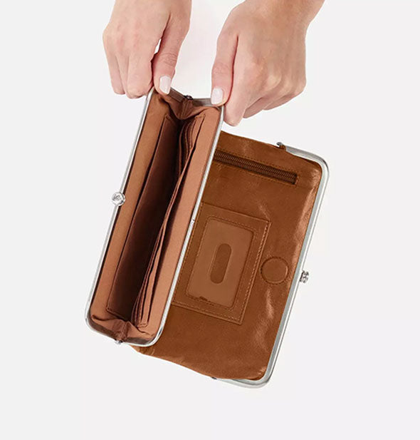 Model's hands hold open one section of a brown leather wallet to reveal card slots inside