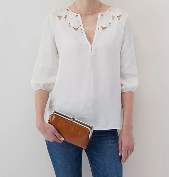 Model wearing jeans and a white shirt holds a brown leather wallet with silver frame hardware for size reference