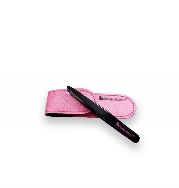 Black tweezer stamped with pink Kelley Baker logo rests on top of a shimmery pink storage case with black Kelley Baker logo