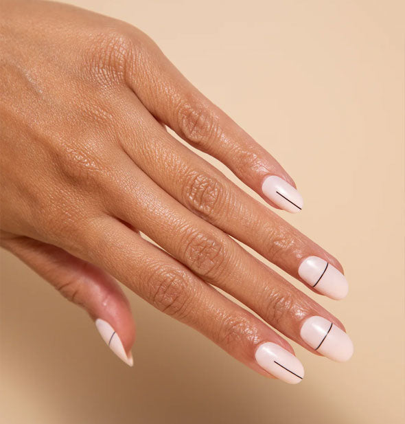 Model's hand wears a set of whitish-pink press on nails which each feature a single thin, black horizontal or vertical line
