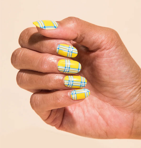 Model's hand wears a set of yellow, blue, and white plaid press-on nails