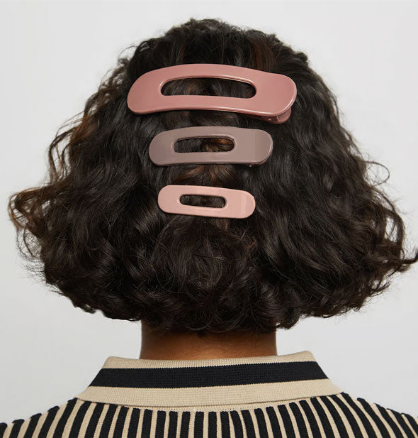 Model wears three blush- and neutral-hued open-shape ovoid clips in descending sizes at the back of a curly bob