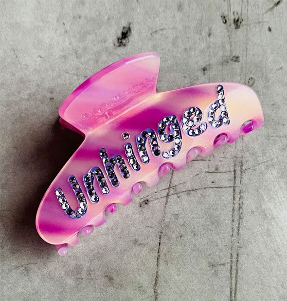 Purplish-pink claw clip says, "Unhinged" in purple lettering accented with purple rhinestones