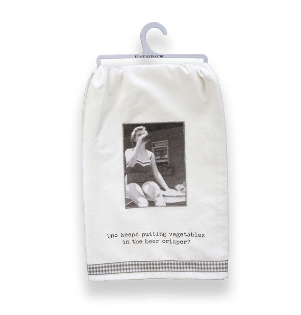 White dish towel on small gray hanger features a retro black and white photograph of a woman in a bathing suit drinking from a bottle above the caption, "Who keeps putting vegetables in the beer crisper?"