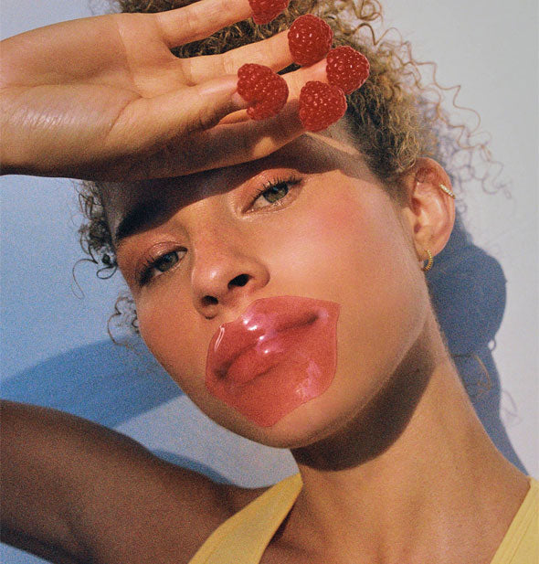 Model with raspberries on her fingertips wears a pink lip-shaped patch over lips 
