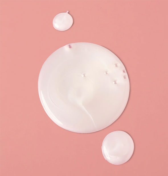 Droplets of white, slightly pearlescent Verb Volume Shampoo on a pink surface