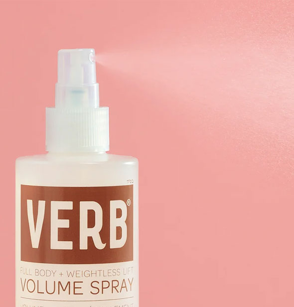 A fine mist of product is dispensed from a bottle of Verb Volume Spray against a pink backdrop