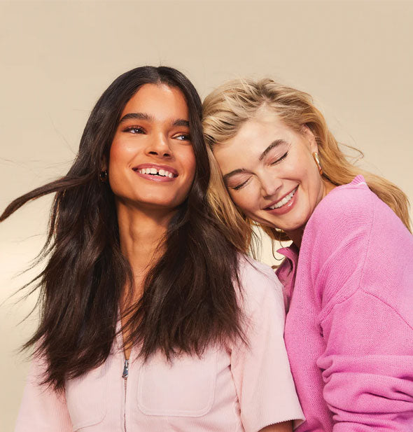 Two smiling models with heads together have thick, full hairstyles