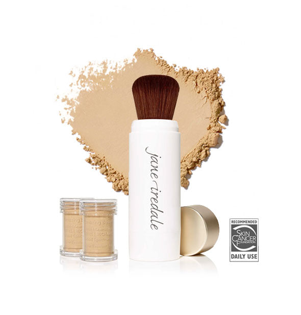 White Jane Iredale powder brush with gold cap removed and set to the side, two refill canisters nearby, and an enlarged product sample in the background in shade Warm Sienna