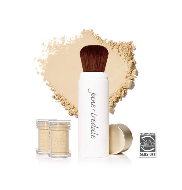 White Jane Iredale powder brush with gold cap removed and set to the side, two refill canisters nearby, and an enlarged product sample in the background in shade Warm Silk