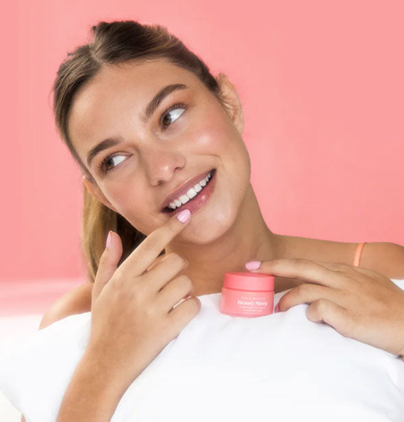 Smiling model clutching pillow applies Watermelon NCLA Beauty brand Beauty Sleep Overnight Lip Mask to lips