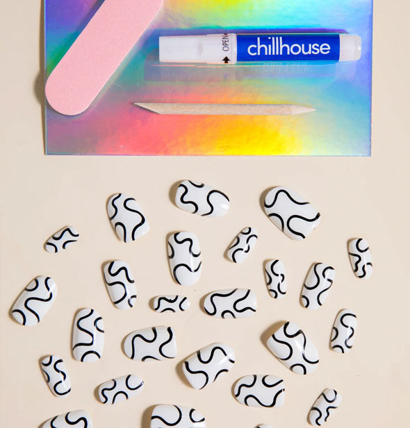 Wavy Baby Chillhouse press on nail pack contents: White nails with black squiggle design, pink file, wooden cuticle pusher, and glue tube