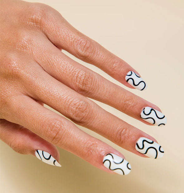 Model's hand wears a set of white press-on nails with a black squiggle design