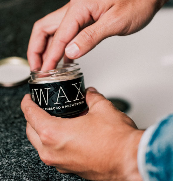 Model dips fingertip into an opened pot of hair styling wax