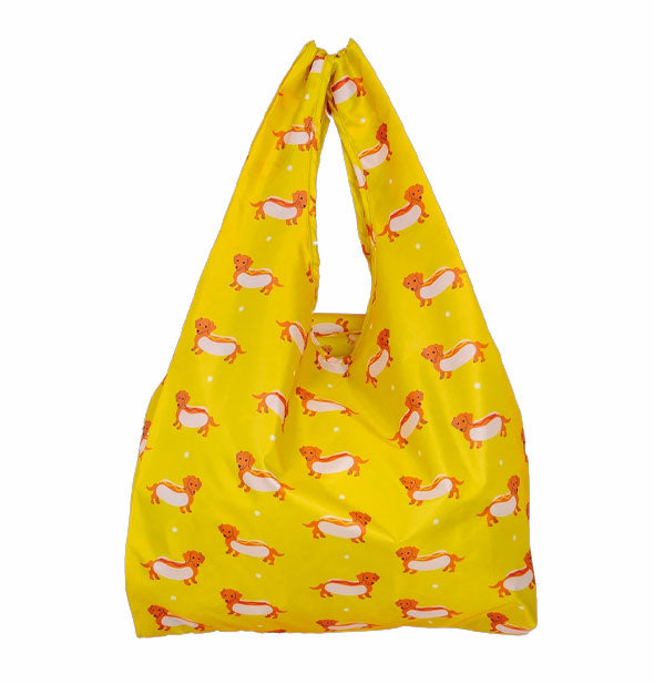 Mustard yellow tote bag with handles pulled together features print of brown Dachshunds in hot dog buns accented by small white polka dots