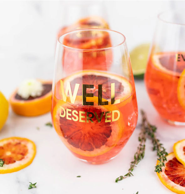 Well Deserved stemless wine glass holds a beverage garnished with citrus slices