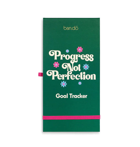 Elongated rectangular green notepad by ban.do with pink elastic band near the bottom says, "Progress Not Perfection Goal Tracker" in white lettering accented by pink and blue flowers