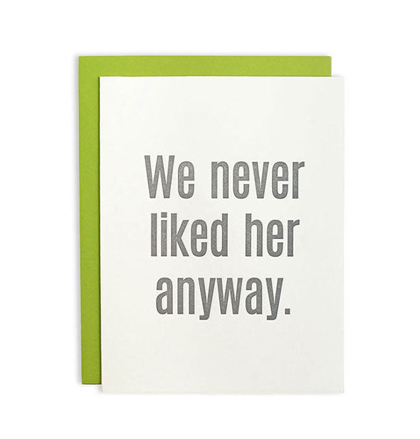 White greeting card with green envelope behind says, "We never liked her anyway" in silver lettering