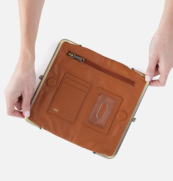 Model's hands hold open a brown leather wallet to show storage compartments inside
