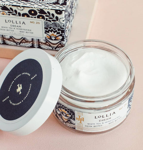 Opened jar of Lollia Dream Body Butter reveals creamy white product inside; lid is set to the side and box is behind